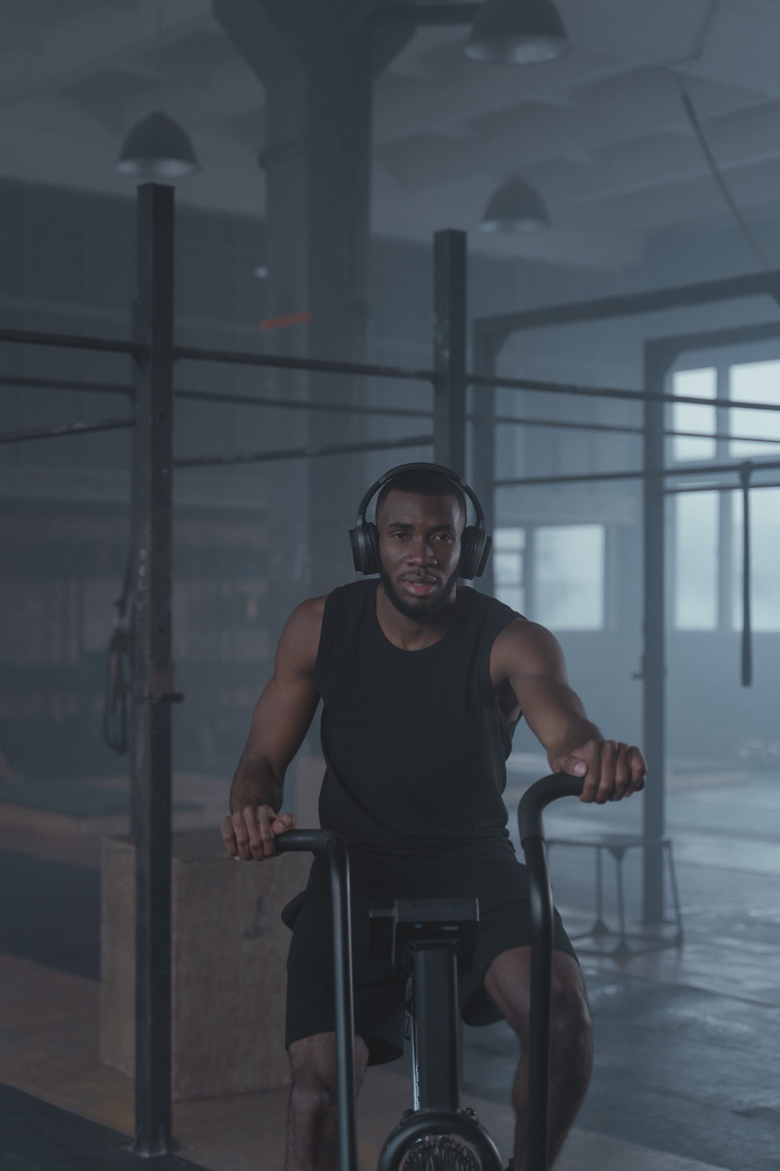 A man in headphones working on an air bike in a hazy warehouse gym