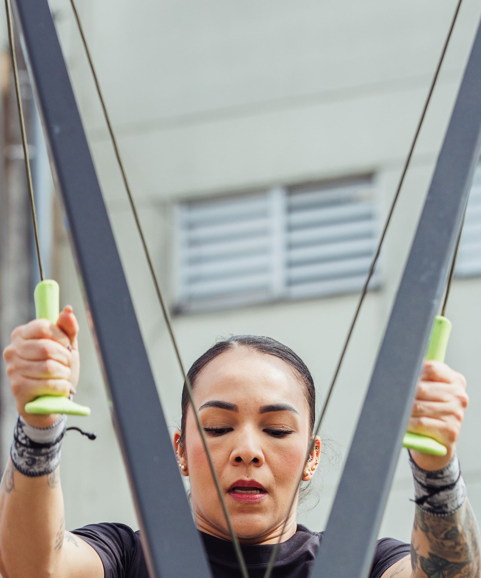 A woman pulling both handles of a ski erg down, eyes lowered, a pale wall behind