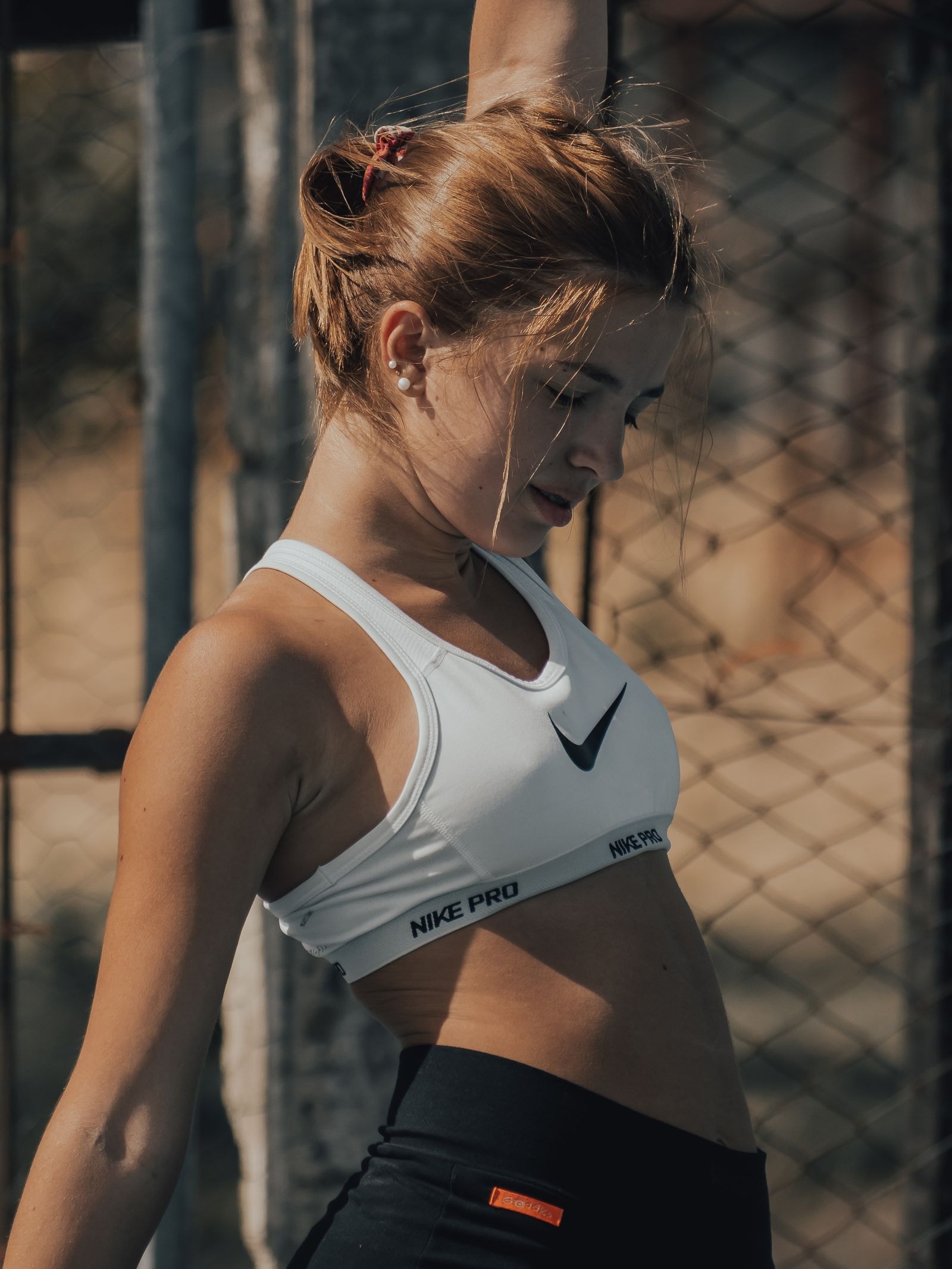 A woman in a white sports bra stretching against a fence
