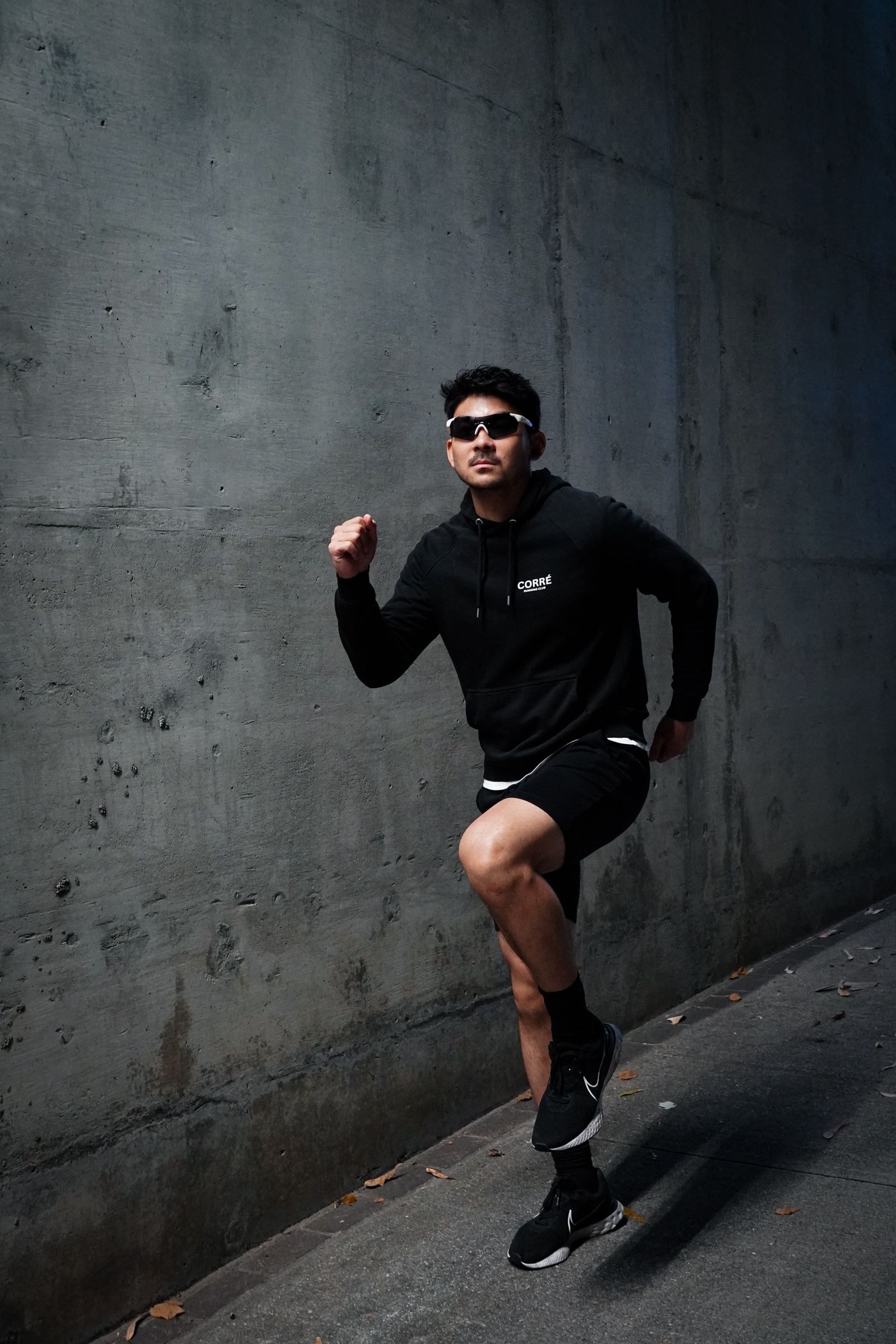 A runner in a black hoodie sprinting past a concrete wall